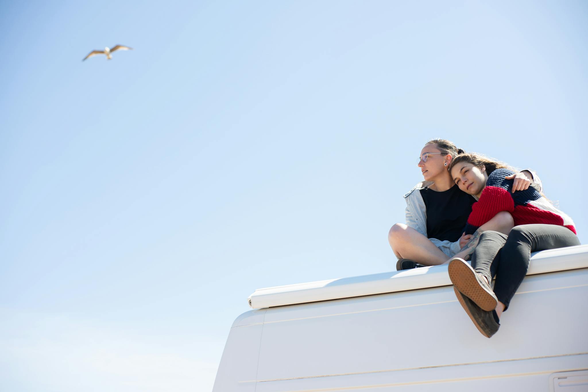 Loving couple sitting on a camper roof enjoying a sunny day, symbolizing freedom and togetherness.